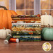 A stack of the fabrics included in the Baskets of Autumn Blessings collection with pumpkins and a basket and a window and thread.