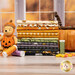 A stack of the fabrics included in the Haunted Acre Wood collection, with  a window and a jar and a poo bear plush and thread and candycorn and a pumpkin basket