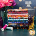 A stack of the fabrics included in the Calico Cat collection with jars and flowers and a bottle and thread and a cat statue.
