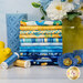 A stack of the fabrics included in the Poppy Serenade collection, with flowers and a jar and a candle and a bird and poppies and thread.