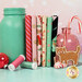 A stack of the fabrics included in the Ginger Cat Christmas collection, with jars and a candycane and ornaments and a gingerbread cookie and peppermints and thread.
