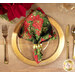 A top down shot of a place setting with the reversible black fabric with red poinsettia fabric of the napkin faced out.