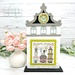 The fully assembled and painted City Clock Tower Cross Stitch Display Backer, staged on a marble countertop with coordinating flowers, displaying a spring cross-stitch project.