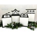 The fully assembled and painted City House Cross Stitch Display Backers #1 - 4, staged on a white tabletop with holiday greenery.