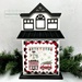 The fully assembled and painted City House #2 Cross Stitch Display Backer, staged on a white tabletop with a decorative garland, displaying a festive cross-stitch project.