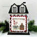 The fully assembled and painted City House #3 Cross Stitch Display Backer, staged on a white tabletop with a decorative garland, displaying a festive cross-stitch project.