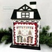 The fully assembled and painted City House #4 Cross Stitch Display Backer, staged on a white tabletop with a decorative garland, displaying a festive cross-stitch project.