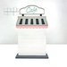 The fully assembled and painted City Cafe Cross Stitch Display Backer, staged on a white tabletop.