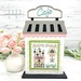 The fully assembled and painted City Cafe Cross Stitch Display Backer, staged on a marble countertop with coordinating flowers, displaying a spring cross-stitch project.