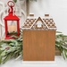 The fully assembled and painted All Seasons Gingerbread House Cross Stitch Display, staged on a wooden tabletop with a frosted wreath and red lantern.