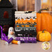 A stack of the fabrics included in the Hauntingly Yours collection, with a window and a haunted house and pumpkins and a ghost and a cat and thread.