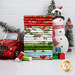 A stack of the fabrics included in the Snowy Greetings collection, with trees and a truck and a snowman and presents and thread.