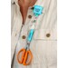 A model wears the scissor lanyard clipped to their shirt lapel, holding a pair of scissors by the protective end to showcase function.