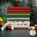 A stack of the fabrics included in the Peppermint & Pine collection, with trees and a wreath and ornaments and peppermint candies and thread.