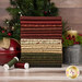 A stack of the fabrics included in the Pineberry Lane collection, with a pinetree and a bell and a candle and thread.