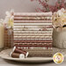 A stack of the fabrics included in the Yardley House Fat Quarter Bundle, with flowers and vases and a candle and a plate and thread.