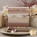 A stack of the fabrics included in the Yardley House Fat Quarter Bundle, with flowers and vases and a candle and a plate and thread.