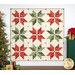 The completed Vintage Stars Quilt colored in Good Tidings fabrics, hung on a white paneled wall bordered by coordinating Christmas furniture and decor.