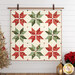 The completed Vintage Stars Quilt colored in Good Tidings fabrics, hung on a white paneled wall bordered by coordinating Christmas furniture and decor.