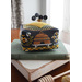 A colorful, cross stitched bee-themed pincushion with buttons reading BUZ sits on stacked vintage books beside a honey dipper.