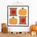 The completed Sew Thankful wall hanging, two spools with pieced leaves paired with two pieced pumpkins in bold autumn colors, hung on a display hanger on a white paneled wall, staged with coordinating spools of thread and autumn decor.