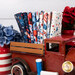 A stack of fabrics included in the Red Truck Road Trip FQ Bundle, in a red truck with flowers and jars and thread.