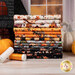 A stack of the fabrics included in the A Haunting We Will Go collection, with pumpkins and a haunted house and a window and thread