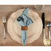 A top down shot of one of the napkins with the light blue fabric faced out, staged on a white plate with cutlery on a wooden table.