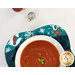 A stylized top-down shot of half the bowl cozy holding a white bowl full of tomato soup. Sparkly ornaments peek into frame from above.