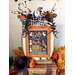 A decorated pumpkin with a cross stitch sign saying Tricks and Treats, surrounded by autumn leaves and decor.