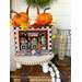 A decorated basket with pumpkins and autumn leaves sits on a table, beside a lantern and beads.