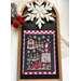 A festive cross stitched winter-themed decoration featuring a stitched scene of St. Nick's tree farm, snowflakes, and a red truck.