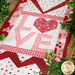 A shot of the center "LOVE" block of the runner demonstrating fabric prints and colors, staged on a wooden tabletop and framed by a green garland.
