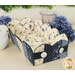 The completed scalloped basket in navy blue, blue and soft white fabrics, staged on a white countertop with coordinating flowers and decor.