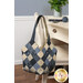 A blue and white patchwork tote bag with floral designs from the Bluebird's Nest collection by Kansas Troubles Quilters, hung on a white chair with coordinating decor.