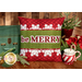 The finished Be Merry pillow wrap kit, a green and red wrap with snowflake borders and appliqué letters that read "Be Merry." The project is staged with a vintage suitcase and coordinating flowers and decor.