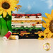 A stack of the fabrics included in the Sunshine Whispers collection, with sunflowers and a green jar and thread and a blue sky.