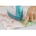 A hand points to a piece of fabric while pressing it with a steam iron on a flat surface.