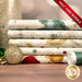 A stack of the five fabrics included in the 5 Half Yard bundle Cream Green/Gold by Stof Fabrics, with ornaments, thread, and a candle.