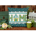 The completed Home Pillow Wrap & Cover, colored in white, teal, and green fabrics. The word "Home" is spelled out in appliqué letters and the "o" is replaced with a tree house. The project is staged with a vintage suitcase and winter themed decor.