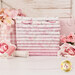 A stack of the fabrics included in the Pretty in Pink collection, with flowers and a mug and a barn window and a pink cannister and thread.