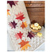 Table runner with patchwork fall leaves resting on a table and wood cabinet.