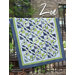 Colorful quilt titled Zoe, featuring geometric patterns in green, blue, and white, displayed outdoors.