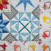 Colorful quilt with various geometric patterns and shapes, including stars and arrows, on a white background.