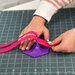 A hand placing a pink zipper strap onto a purple hexagonal zipper jig.