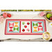 The completed Sew Cute Runner - September table topper, staged on a white dresser, accented with apples, a spool of thread, and flowers. 
