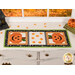 The completed Sew Cute Runner - October table topper, staged on a white dresser, accented with scattered candy corn, a stack of spooky books and a haunted house statue sitting in the top left corner. 