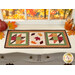 The completed Sew Cute Runner - November table topper, staged on a white dresser, accented with scattered leaves, a pumpkins and a drink of apple cider in the upper right corner. 