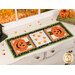 The completed Sew Cute Runner - October table topper, staged on a white dresser, accented with scattered candy corn, a stack of spooky books and a haunted house statue sitting in the top left corner. 