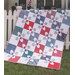 A colorful patchwork quilt draped over a white fence, featuring red, blue, and white floral patterns.